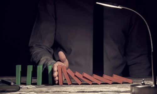 Person stoppt Dominoeffekt als Symbol für Prävention