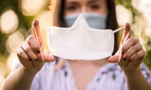 Frau hält eine Gesichtsmaske vor sich, betonend auf Prävention