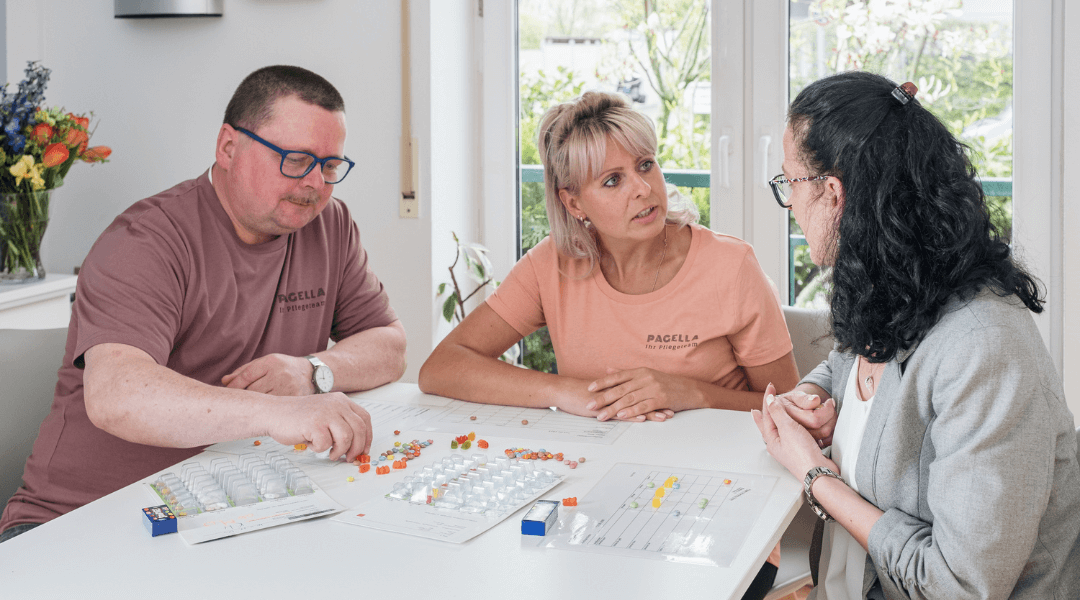 Drei Mitarbeiter des Pagella Pflegedienstes sitzen gemeinsam an einem Tisch, analysieren einen Plan und besprechen wichtige Details.