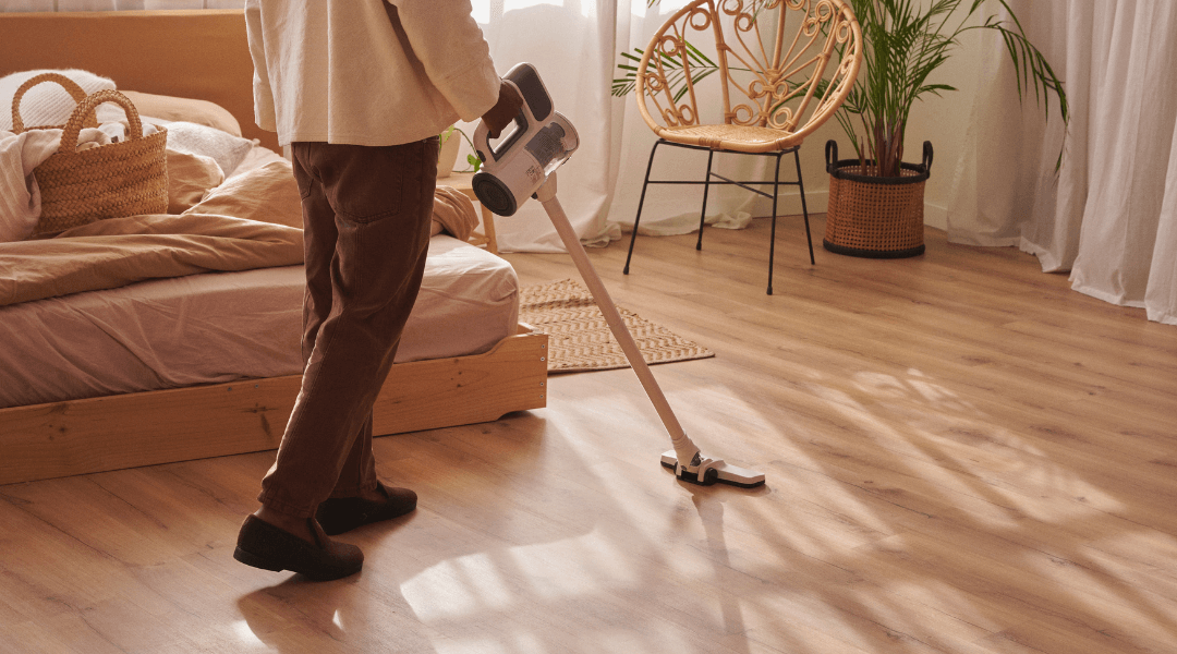 Person beim Staubsaugen in einem gepflegten Schlafzimmer, symbolisiert Unterstützung bei der Haushaltsreinigung.