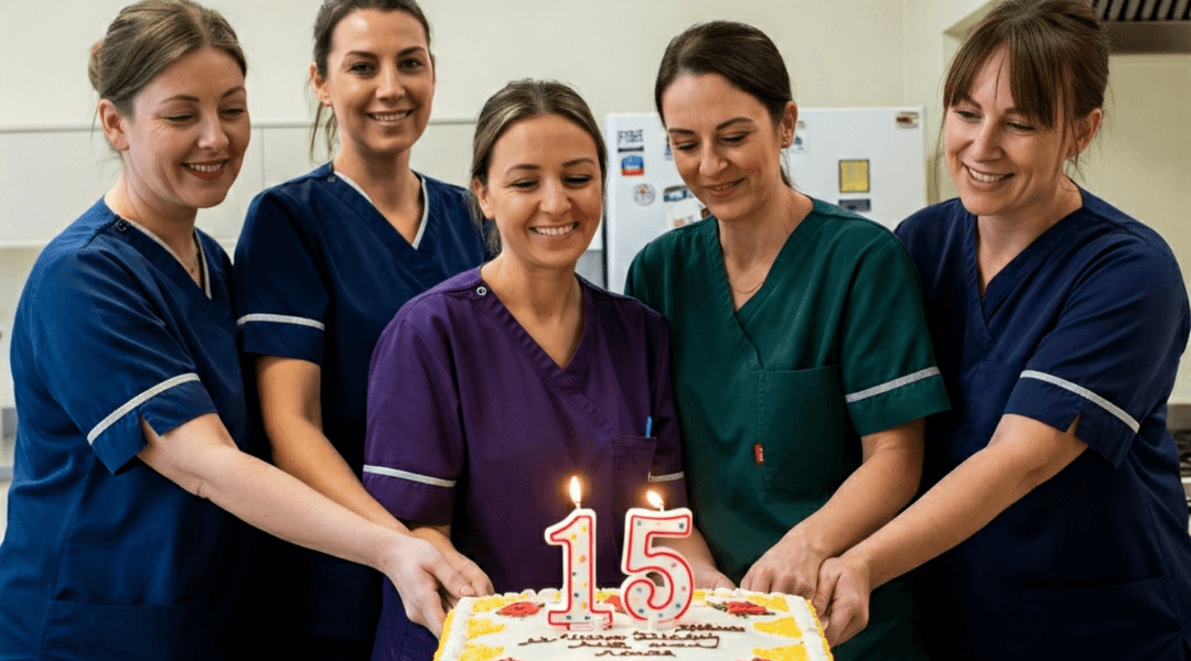 Ein Team von Pflegekräften des Pagella Pflegedienstes feiert 15 Jahre Bestehen mit einer Torte in der Küche.