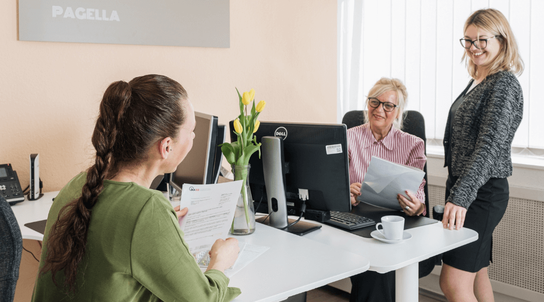 Drei freundliche Mitarbeiterinnen von Pagella Pflegedienst im Büro, die ein Beratungsgespräch führen.