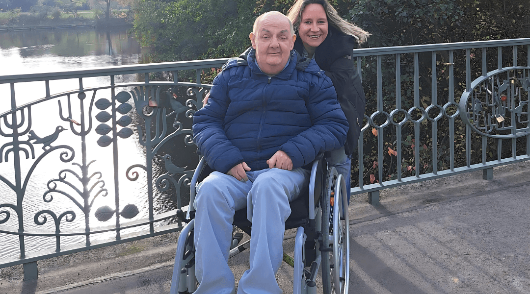 Ein Senior im Rollstuhl und eine Betreuerin genießen gemeinsam einen Spaziergang in Berlin.