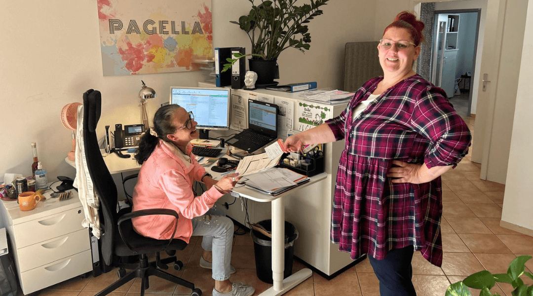 Zwei Mitarbeiterinnen des Pagella Pflegedienstes bei der Bearbeitung von Dokumenten und der Betreuung von Anliegen.