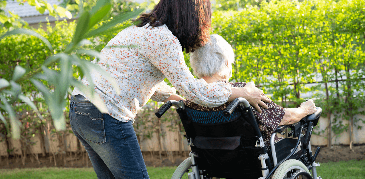 Seniorin im Rollstuhl wird von einer Betreuungskraft geschoben